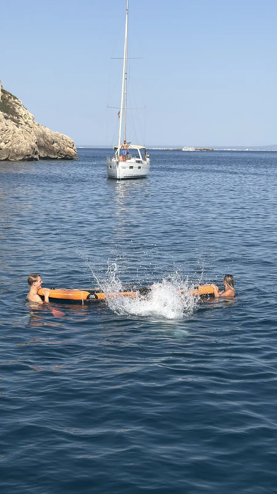 A big splash as the guest drops off the paddleboard into the water, with the yacht at anchor in the background