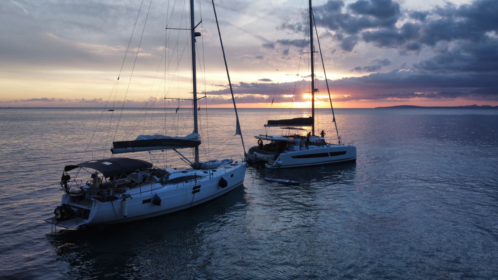 Sailing yacht and catamaran anchored together at sunset