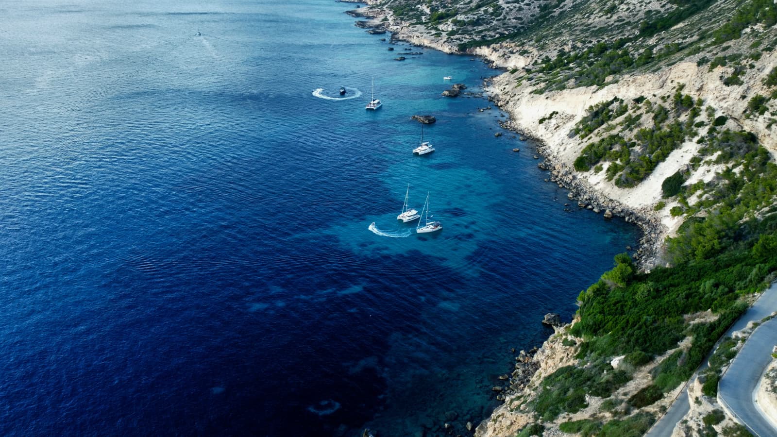 Aerial view of yachts exploring a rugged Mallorcan coastline