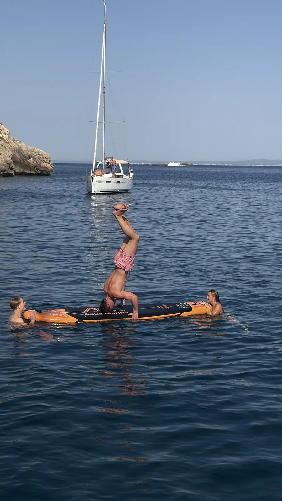The guest holds a headstand on the paddleboard while the two swimmers keep it steady