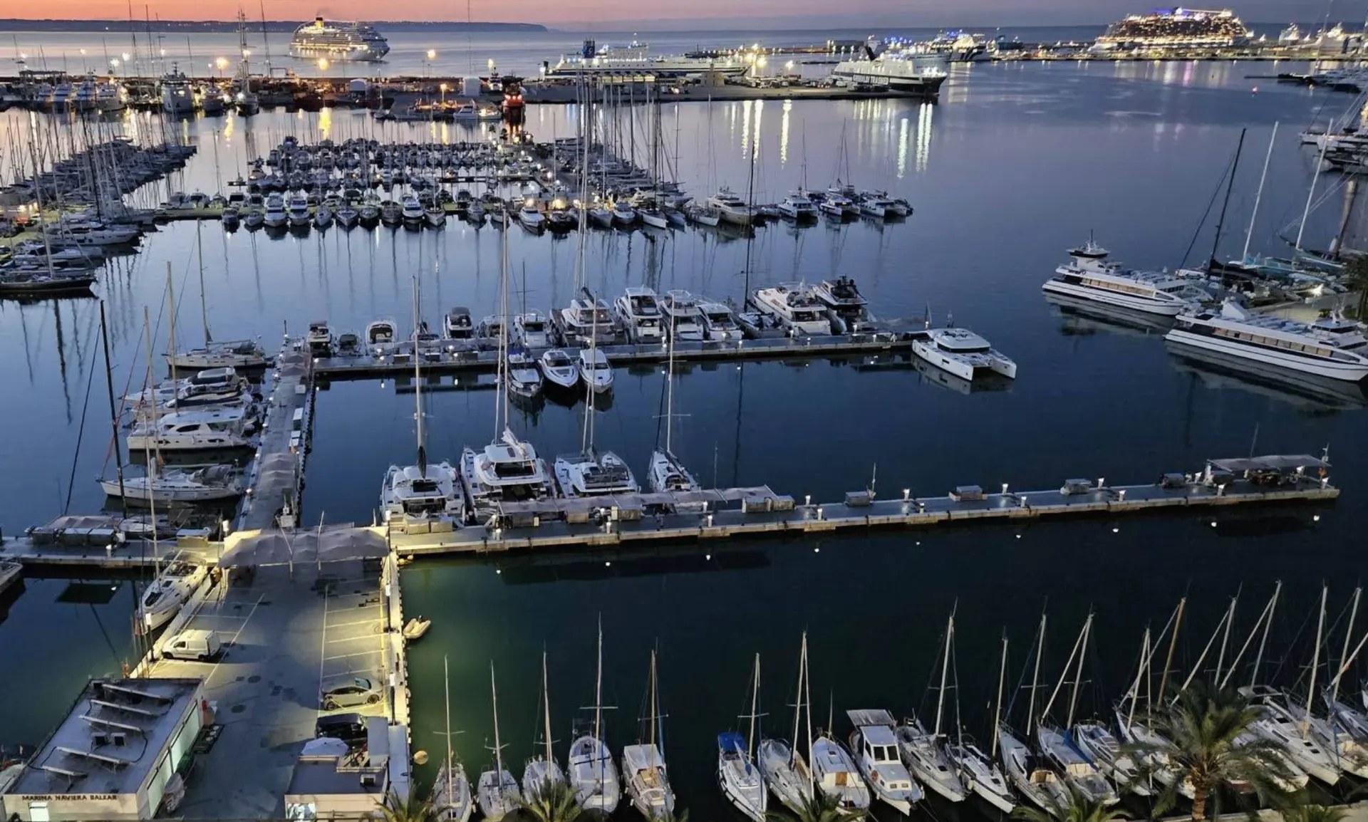 Marina Naviera Balear at dusk in Palma, with yachts, catamarans and the port lights reflecting on the water